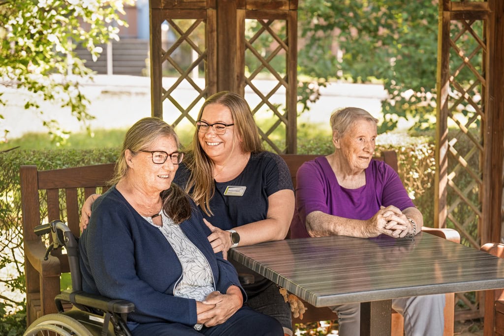 Pflegerin sitzt mit zwei älteren Frauen im Garten