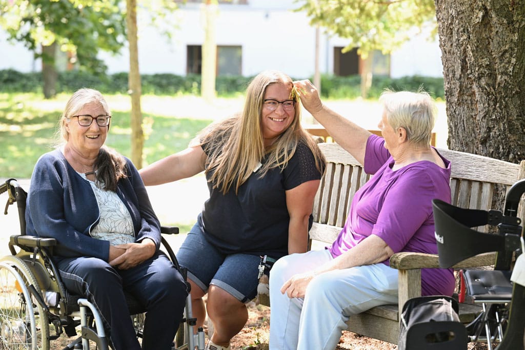 Pflegerinn mit zwei aelteren damen sitzt im garten